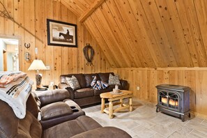 A cozy room with a wooden ceiling, a leather sofa, a wooden table, and a wood-burning stove.