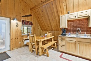 A wooden interior with a dining table, benches, and a kitchen area with wooden cabinets and a sink.