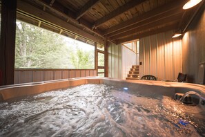 A hot tub with a wooden interior, a window with a view of trees, and a chair near the window. - Woodland view-Hitchin' Post (Laurelville)