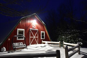 A snow-covered barn with a wooden fence and a bench.