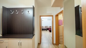 A hallway with a dark wooden cabinet, a black refrigerator, and a wooden door leading to a living area with a sofa and a pink cabinet.