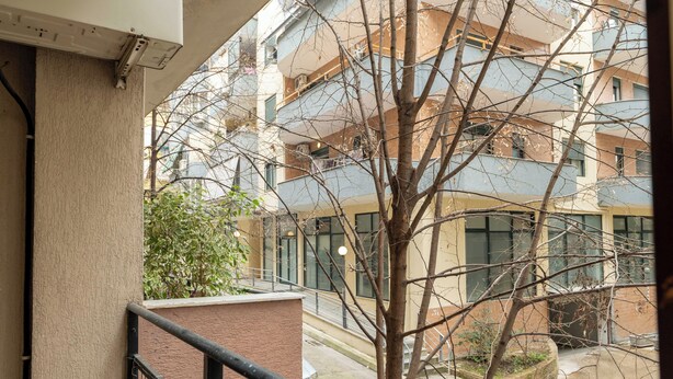 A view from a balcony overlooking a multi-story building with balconies, a tree, and a street below.