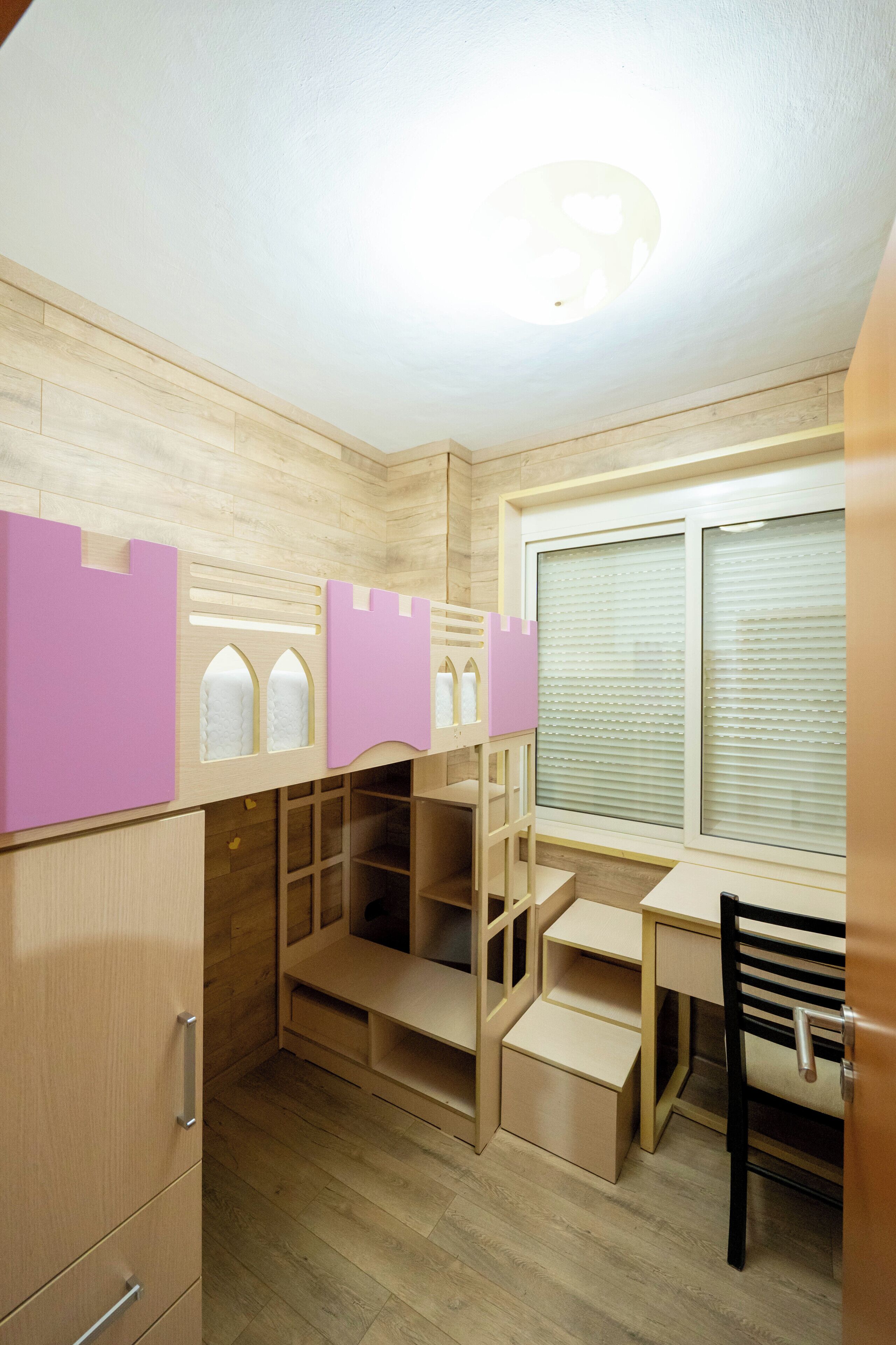 Una habitación infantil con literas, un escritorio y una ventana con persianas.