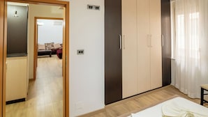 A bedroom with a bed, a wardrobe, a mirror, and a door leading to another room.