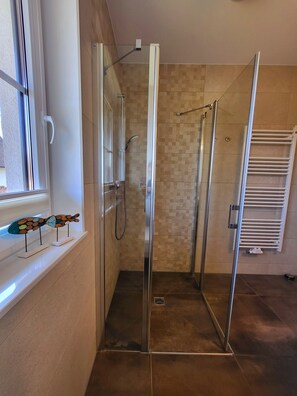 A glass-enclosed shower with a tiled floor, a window with a decorative fish sculpture, and a white towel rack. - Stunning beachfront vacation apartment with a fireplace, in a quiet location (Dranske)