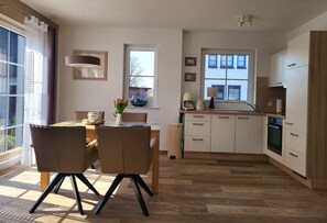 A modern kitchen with wooden flooring, white cabinets, and a dining area with two chairs and a table. - Stunning beachfront vacation apartment with a fireplace, in a quiet location   (Dranske)