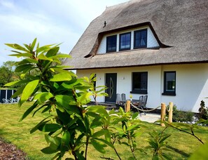 A house with a thatched roof, a front porch with a table and chairs, and a well-maintained lawn. - Stunning beachfront vacation apartment with a fireplace, in a quiet location (Dranske)