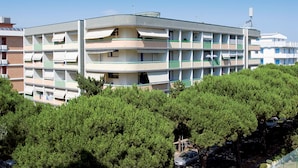 A multi-story building with balconies, surrounded by dense green trees. - Ideal Getaway Apartment for Groups in Bibione (San Michele al Tagliamento)