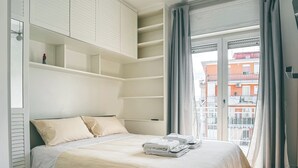 A bedroom with a bed, built-in shelving, a hanging light fixture, and a view of buildings through a window. - I Ludovici Luxury B&B (Casoria)