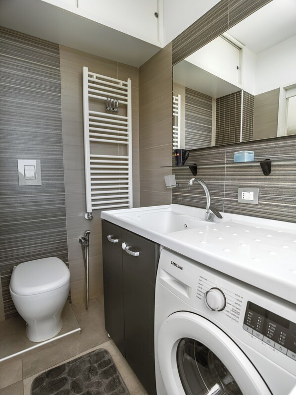 A modern bathroom with a built-in washing machine, a toilet, and a towel rack. - I Ludovici Luxury B&B (Casoria)