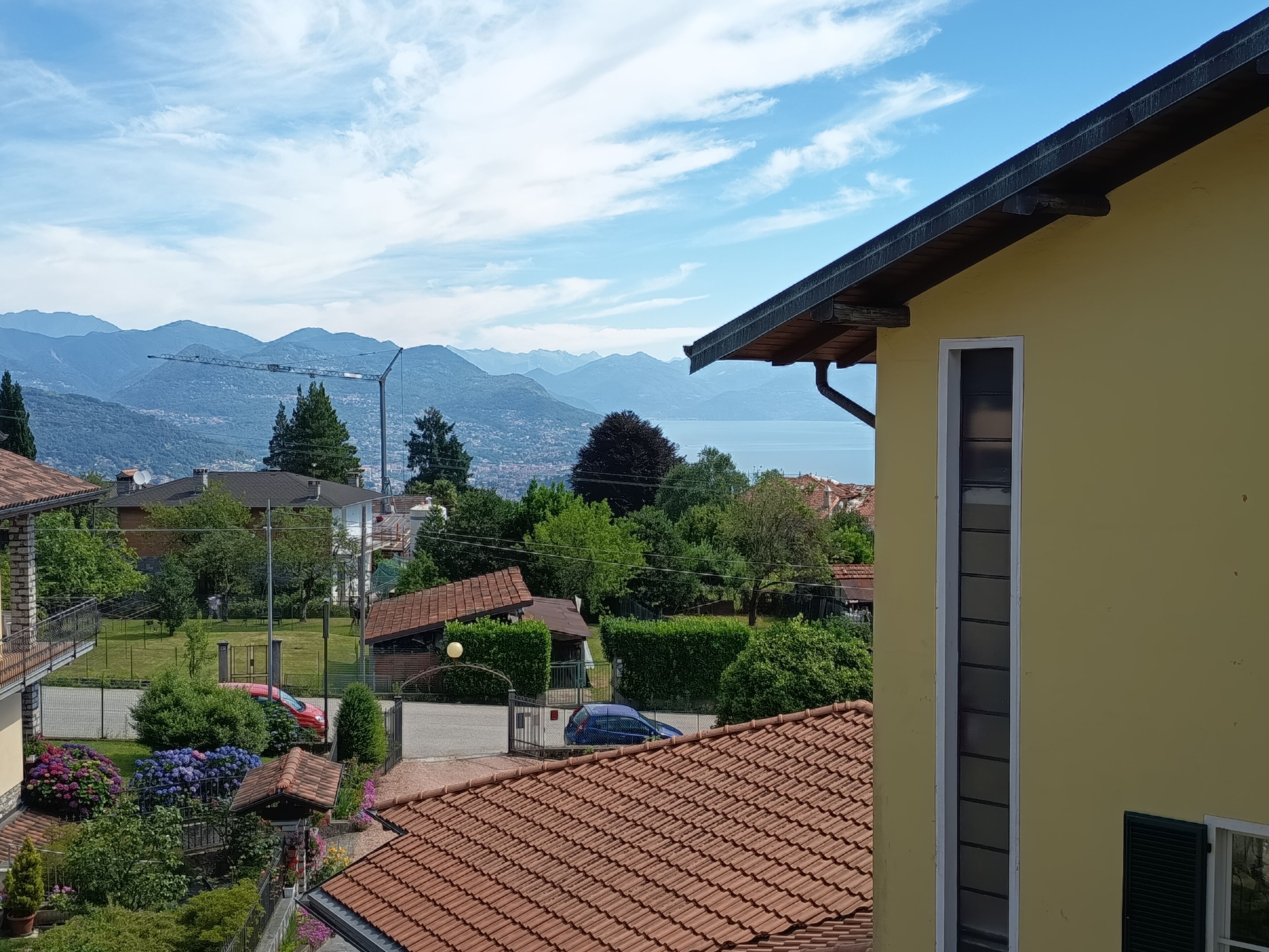 A residential area with a yellow building, red-tiled roofs, and a view of mountains and a lake.