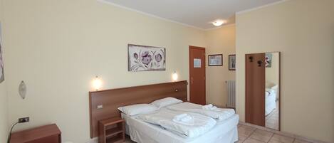A hotel room with a bed, bedside table, chair, and a mirror.