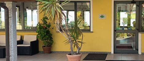 A building entrance with a tiled roof, a potted plant, a bench, and a door with a glass panel.