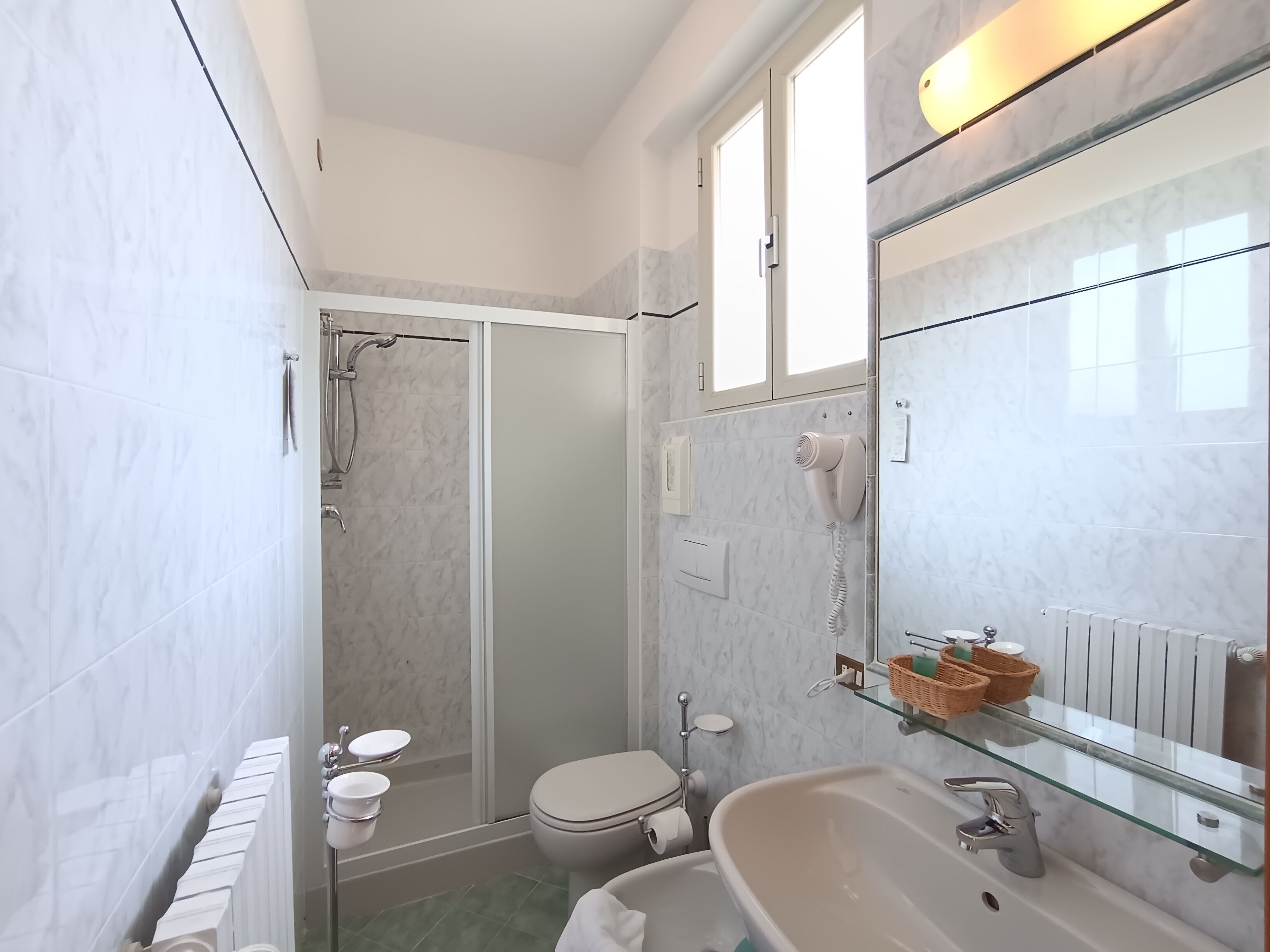 Un baño moderno con cabina de ducha de vidrio, inodoro, lavabo con repisa de vidrio y espejo.
