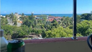 Une vue depuis un balcon, avec un ciel bleu dégagé, un océan à l’horizon et quelques touches de verdure.