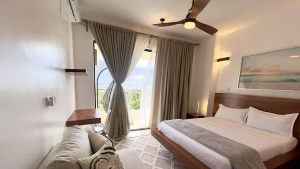 Une chambre d’hôtel avec un lit, un canapé, un ventilateur de plafond et une fenêtre avec des rideaux.