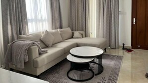 Un salon moderne avec un canapé d’angle beige, une table basse ronde et un tapis à motifs.
