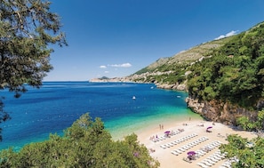 A coastal beach with clear blue waters, a sandy shore, and a row of sun loungers.