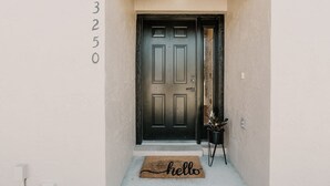 Una porta negra amb un felpú que diu "hello" i una petita planta en test amb ella.