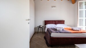 A bedroom with a wooden ceiling, a bed with a red headboard, white bedding, and a small bedside table with a book and glasses. - Corte Fasanella 50 in Toscolano Maderno (Toscolano Maderno)