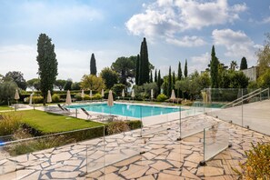 A swimming pool surrounded by stone tiles, with lounge chairs and umbrellas. - Corte Fasanella 50 in Toscolano Maderno (Toscolano Maderno)