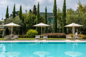 A swimming pool with lounge chairs and umbrellas, surrounded by tall trees and greenery. - Corte Fasanella 50 in Toscolano Maderno (Toscolano Maderno)