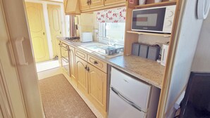 Une cuisine compacte avec des meubles en bois, un four à micro-ondes encastré, un grille-pain et un petit réfrigérateur.