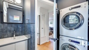 Une buanderie moderne équipée d’un grand lave-linge et d’un sèche-linge, d’un évier avec un miroir et d’une porte donnant sur l’espace de vie.