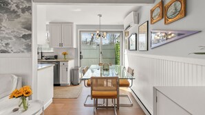 Une cuisine moderne avec des meubles blancs, une table à manger en verre et un luminaire suspendu.