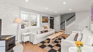 Un salon moderne avec un canapé blanc, une table basse en bois et un tapis à carreaux. On y trouve une cheminée, une lampe et un tableau accroché au mur.