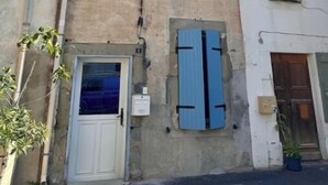 A building with a white door, two windows with blue shutters, and a small balcony. - La Maison de Sainte-Eulalie (Roubia)