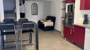 A modern kitchen with red cabinets, a dining area with a table and chairs, and a staircase leading to an upper level. - La Maison de Sainte-Eulalie (Roubia)