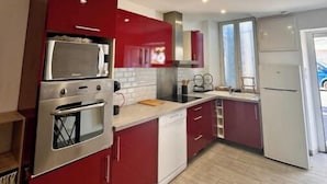 A modern kitchen with red cabinets, stainless steel appliances, and a white dishwasher. - La Maison de Sainte-Eulalie (Roubia)