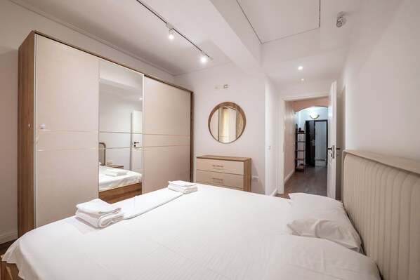 Una habitación de hotel moderna con una cama grande, un armario, una mesita de noche y un espejo.