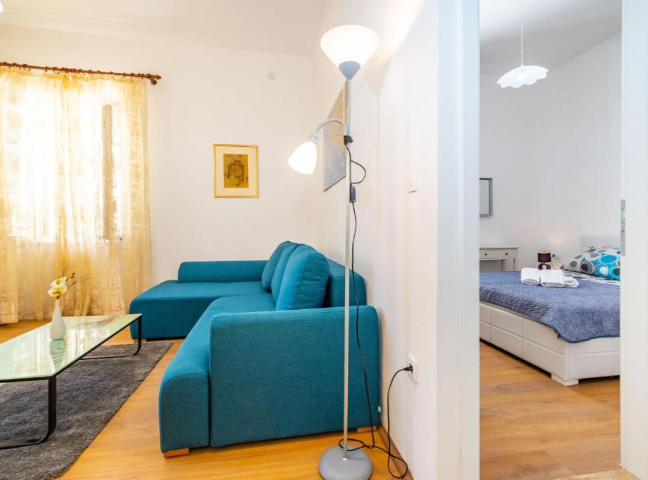 Una sala de estar moderna con un sofá azul, una mesa de centro de vidrio y una lámpara de pie.