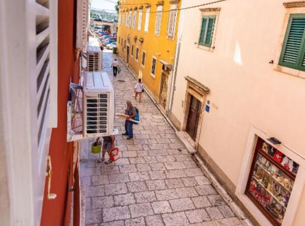 Una estrecha calle adoquinada flanqueada por edificios, un hombre cargando un objeto grande y una tienda con escaparate.