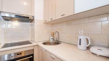 A modern kitchen with white cabinets, a stainless steel sink, a built-in oven, and a kettle.
