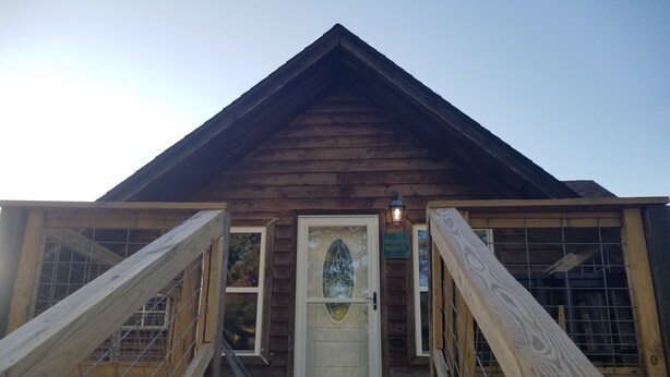 Une cabane en bois avec une porte blanche, un petit porche et un escalier en bois menant à l’entrée.