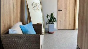 A hallway with a wicker sofa, a potted plant, a wall clock, and a wooden door. - Treeloft 29 (Girón)