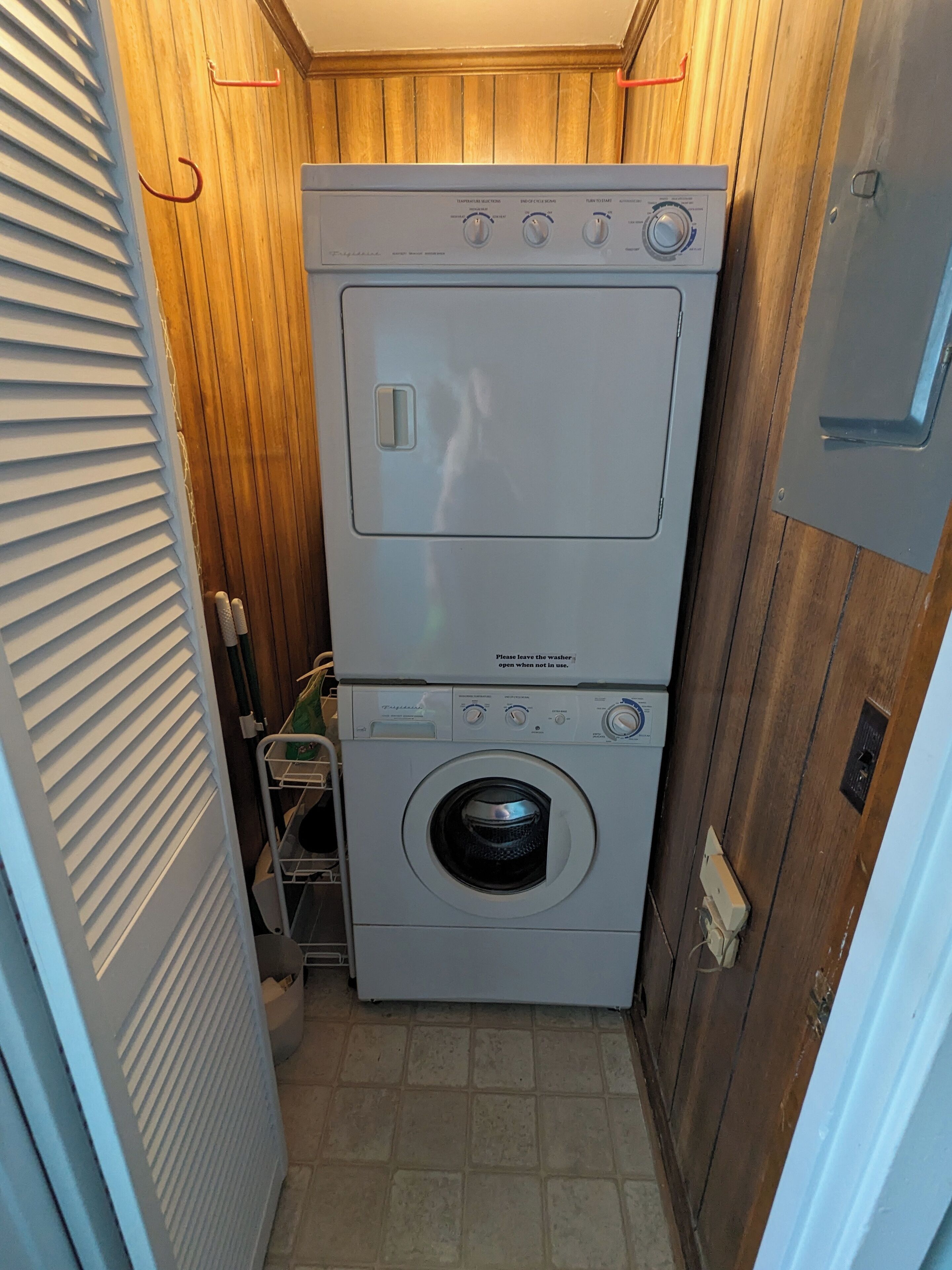 Une petite buanderie avec une machine à laver et un sèche-linge superposés, des murs en bois et un sol carrelé.