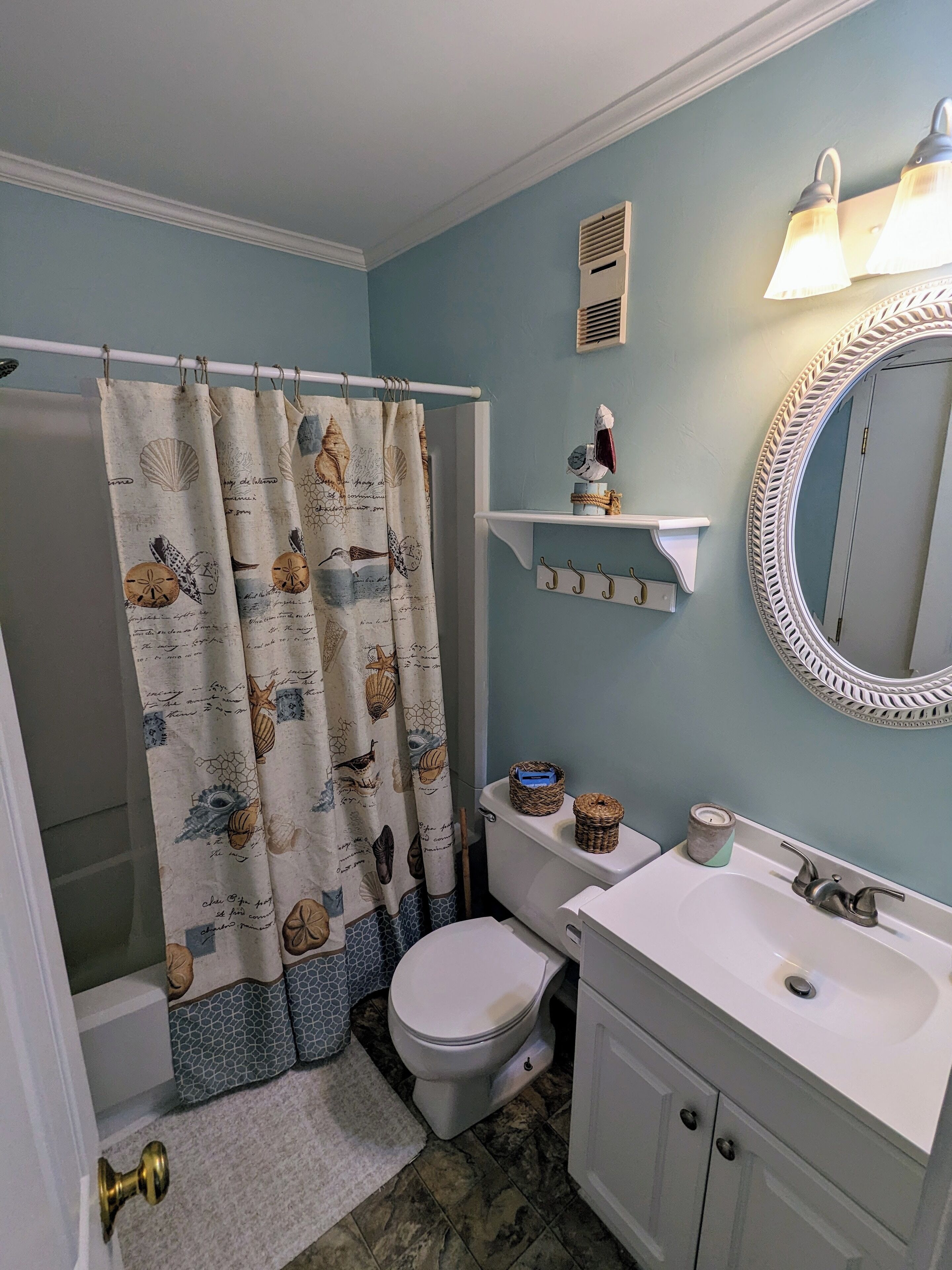 A bathroom with a shower curtain featuring sea creatures, a toilet, a sink with a mirror, and a shelf with decorative items.