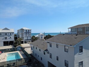 A residential area with a swimming pool, multiple houses, and a view of the ocean. - Ocean View Condo with Pool in Carolina Beach—2 bedroom/2 bath—balcony (Carolina Beach)