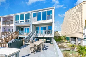 Ein mehrstöckiges Anwesen direkt am Strand mit Balkonen, Gartenmöbeln und einer überdachten Terrasse.