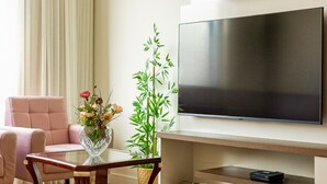 Un salon moderne avec un téléviseur à écran plat fixé au mur, un fauteuil rose, une table basse en verre ornée d’un vase à fleurs et une plante en bambou.