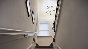 A staircase with carpeted steps, white handrails, and a chandelier at the top.