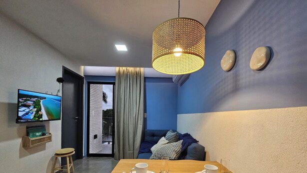 Ein modernes Wohnzimmer mit Essbereich, einem an der Wand befestigten Fernseher und Blick ins Freie durch eine Schiebetür.