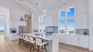 Una cocina amplia con una isla grande, armarios blancos y una zona de bar con taburetes.