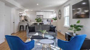 A modern living room with a grey sofa, blue chairs, a coffee table, and a TV on the wall. - Near Ravinia and Navy Base, charming 3-bedroom house in peaceful Highland Park (Highland Park)