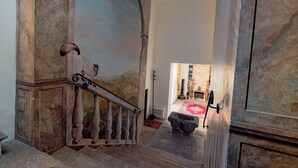 A grand staircase with marble walls and a mural, leading to a room with a red carpet and a stone bench. - The Prince's "Casena" - Historic home with a sea view (Palermo)