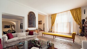 A living room with a sofa, coffee table, and a bench. There is a large painting on the wall and a window with curtains. - The Prince's "Casena" - Historic home with a sea view (Palermo)